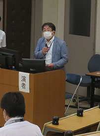講義台でマイクを持ち発表を行っている様子。