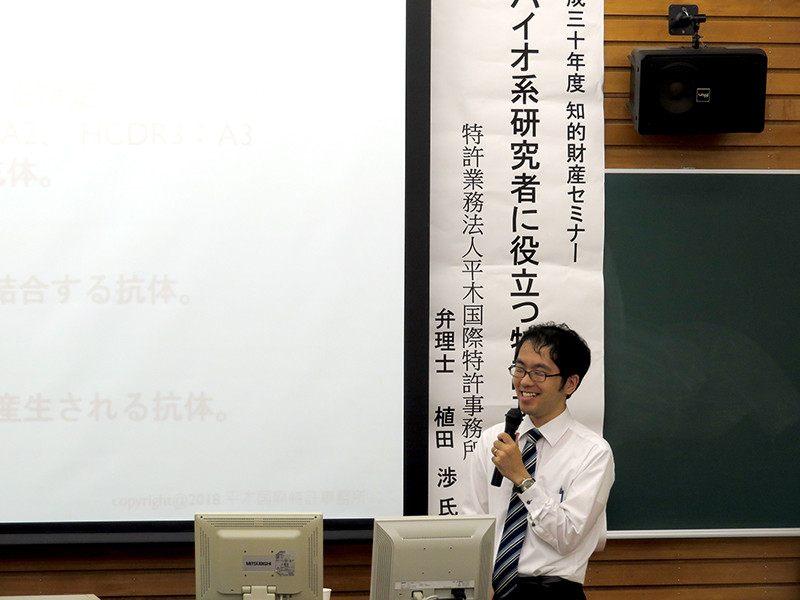 知的財産セミナーで講演する植田氏がマイクを持ち、聴衆に向けて話している様子。