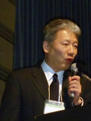 スーツを着た男性がマイクを持ってスピーチをしている