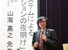男性がマイクを持って講演を行っている