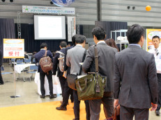 スーツ姿の人々が展示会場で列を作っている