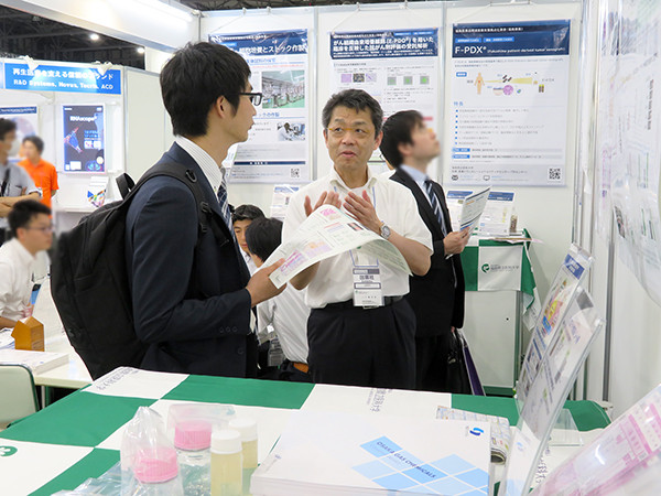 展示ブース内で資料を手にする来場者にスタッフが説明する様子