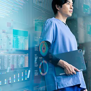 医療現場でデータを分析する医師が、タブレットを持ちながらモニターを見つめている様子。