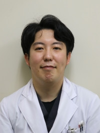 園部樹助教がネームプレートを首から下げてまじめな表情をしているポートレート。