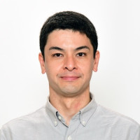 福島県立医科大学の助手、小河原崚氏のポートレート写真。白衣を着て微笑む姿。