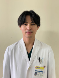 福島県立医科大学の腫瘍内科学講座主任教授、佐治重衡氏のポートレート。白衣を着用し、背景には書類や小物が並ぶ。