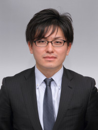 福島県立医科大学の腫瘍内科学講座主任教授、佐治重衡氏のポートレート。白衣を着用し、背景には書類や小物が並ぶ。