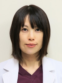 医療白衣を着た女性が微笑んでいるポートレート。背景は淡い青色。