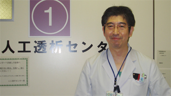 人工透析センターの前で白衣を着た男性が微笑んでいる写真。