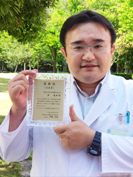 医師が表彰状を持ち、緑豊かな公園で微笑んでいる様子。