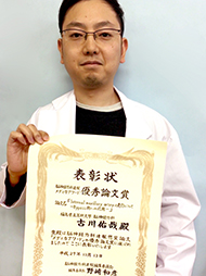 表彰状を持つ医師が白衣を着ている写真。
