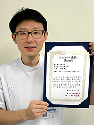 医療従事者が賞状を持って微笑んでいる写真。福島県立医科大学に関連する内容。
