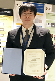 福島県立医科大学の岩舘学講師が、研究成果を示す賞状を持って微笑んでいる写真。