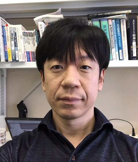 福島県立医科大学の研究者、志賀哲也氏が書斎で自撮りをしている様子。背景には書籍が並んでいる。