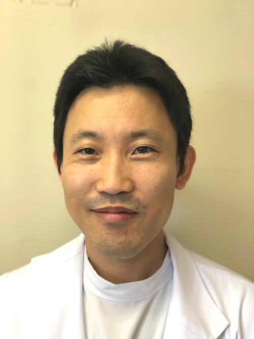 岡山洋和講師が白衣を着て微笑んでいるポートレート。