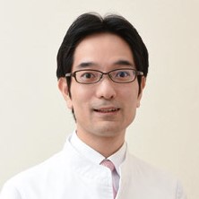 医療白衣を着た男性が微笑んでいるポートレート。眼鏡をかけ、清潔感のある背景で撮影。