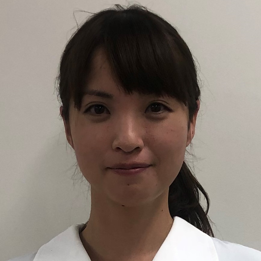 医療白衣を着た女性が微笑んでいるポートレート。背景は無地の壁。