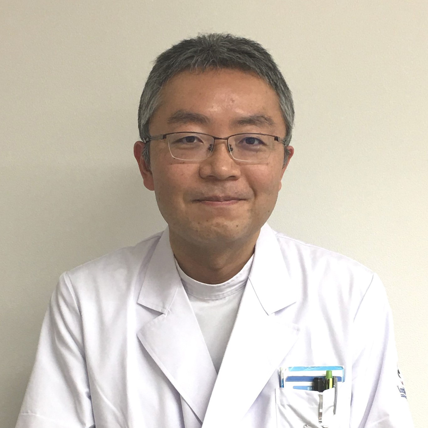 医療白衣を着た男性が微笑んでいるポートレート。背景は無地の壁。