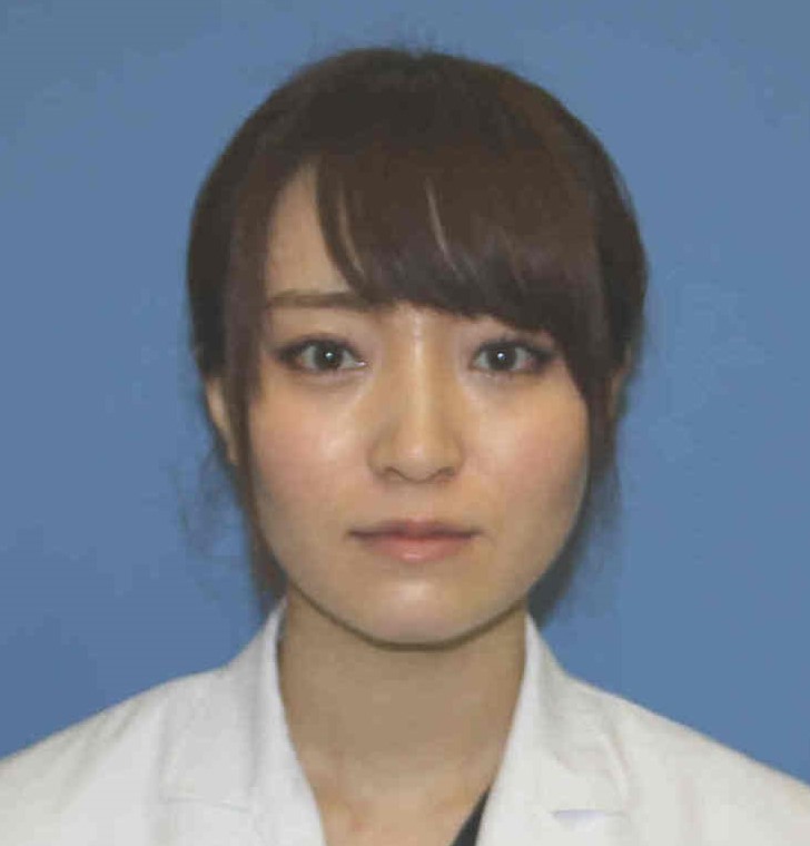 医療用白衣を着た女性のポートレート。背景は青色で、真剣な表情を浮かべている。