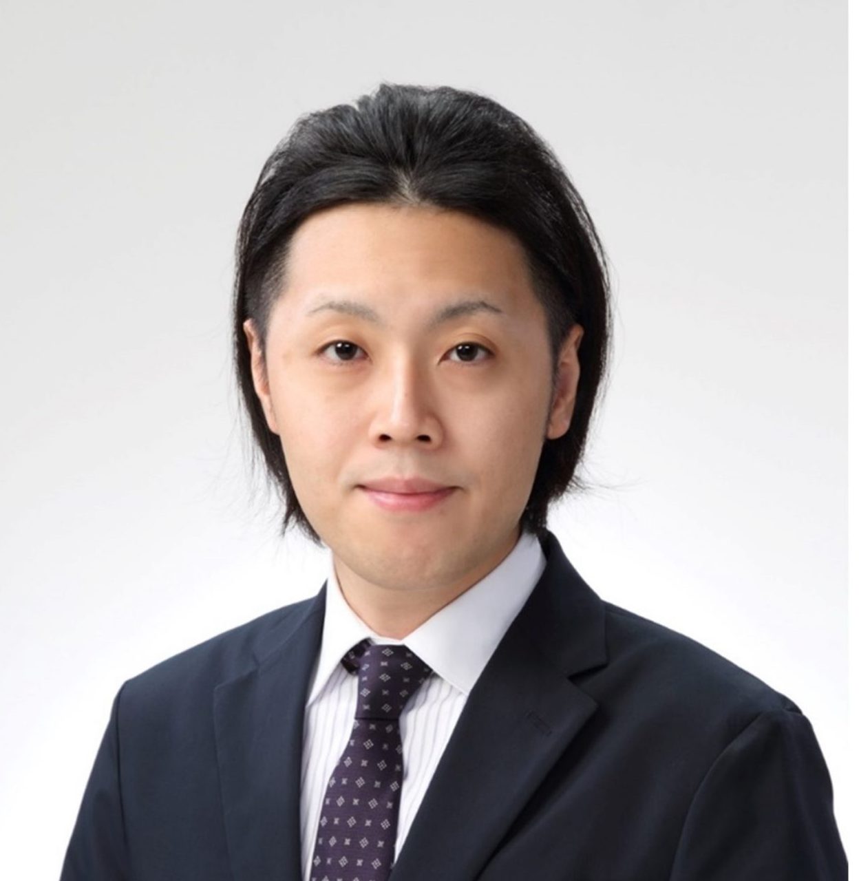 松田将門助教のポートレート写真。スーツを着用し、真剣な表情でカメラを見つめている。
