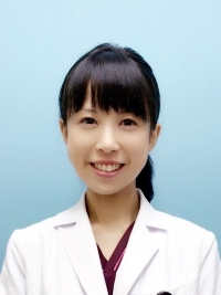 医療白衣を着た女性が微笑んでいるポートレート。背景は淡い青色。