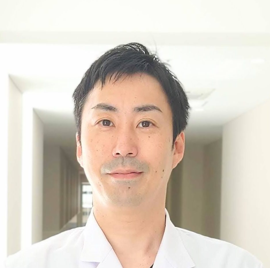 福島県立医科大学の薬剤部で働く男性が、明るい廊下で微笑んでいるポートレート。