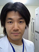 医療現場で白衣を着た男性の自撮り写真。背景には医療機器が見える。