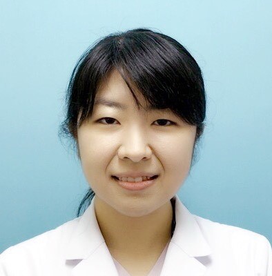 医療用白衣を着た女性が青い背景の前で微笑んでいるポートレート。