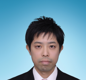 吉江進助教の公式プロフィール写真。青い背景の前でスーツを着た男性。