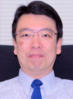医学部の教授、河野浩二氏のポートレート。白いシャツにネクタイを着用し、微笑んでいる。