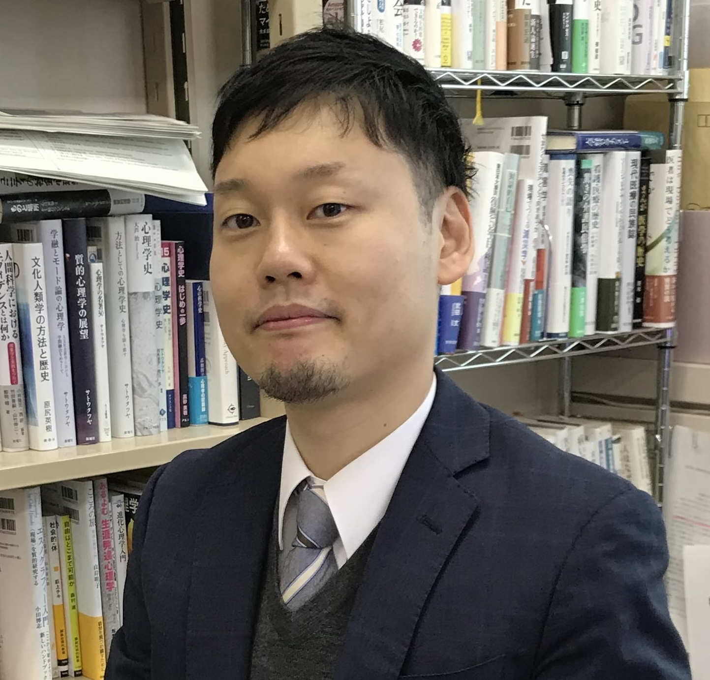 福島県立医科大学の講師、日高友郎氏が書籍の前で微笑んでいる写真。