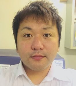 医学部の講師、町田豪氏のポートレート。白いシャツを着て、真剣な表情でカメラを見つめている。