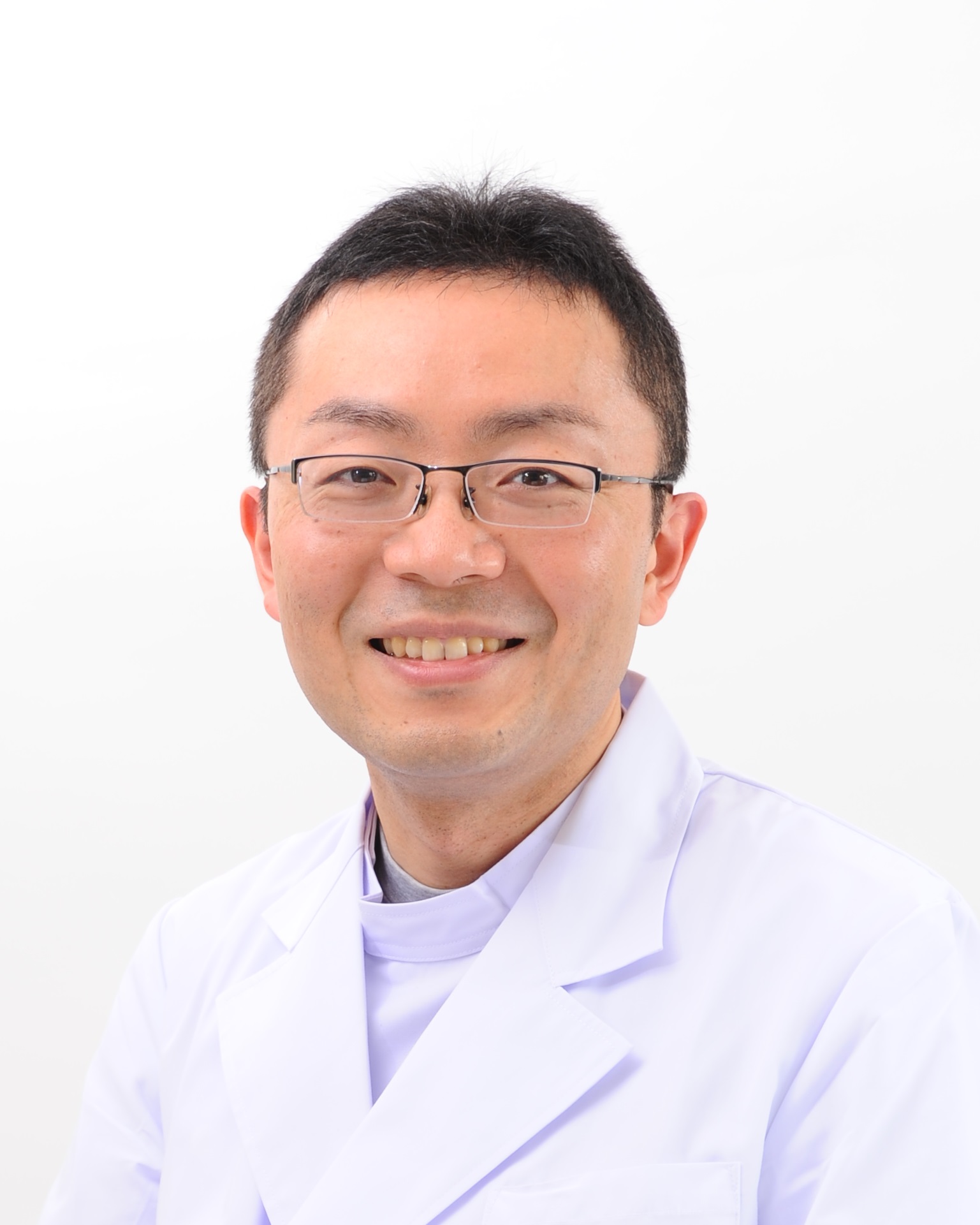 医療白衣を着た男性が微笑んでいるポートレート。背景はシンプルで明るい。