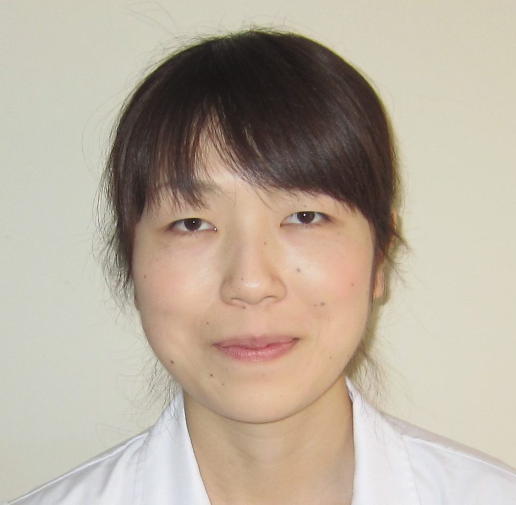 医療従事者の女性が白衣を着て微笑んでいるポートレート。背景は淡い色合い。