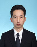 金城貴士准教授の公式なプロフィール写真。スーツを着用し、青い背景の前で真剣な表情を浮かべている。