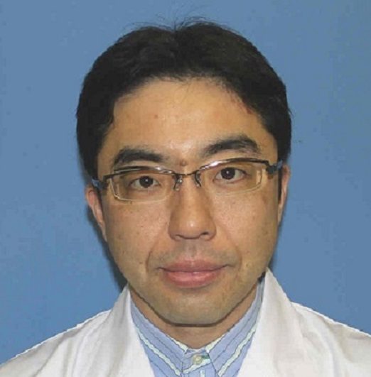 医療用白衣を着た男性のポートレート。背景は青色で、眼鏡をかけた表情が穏やか。