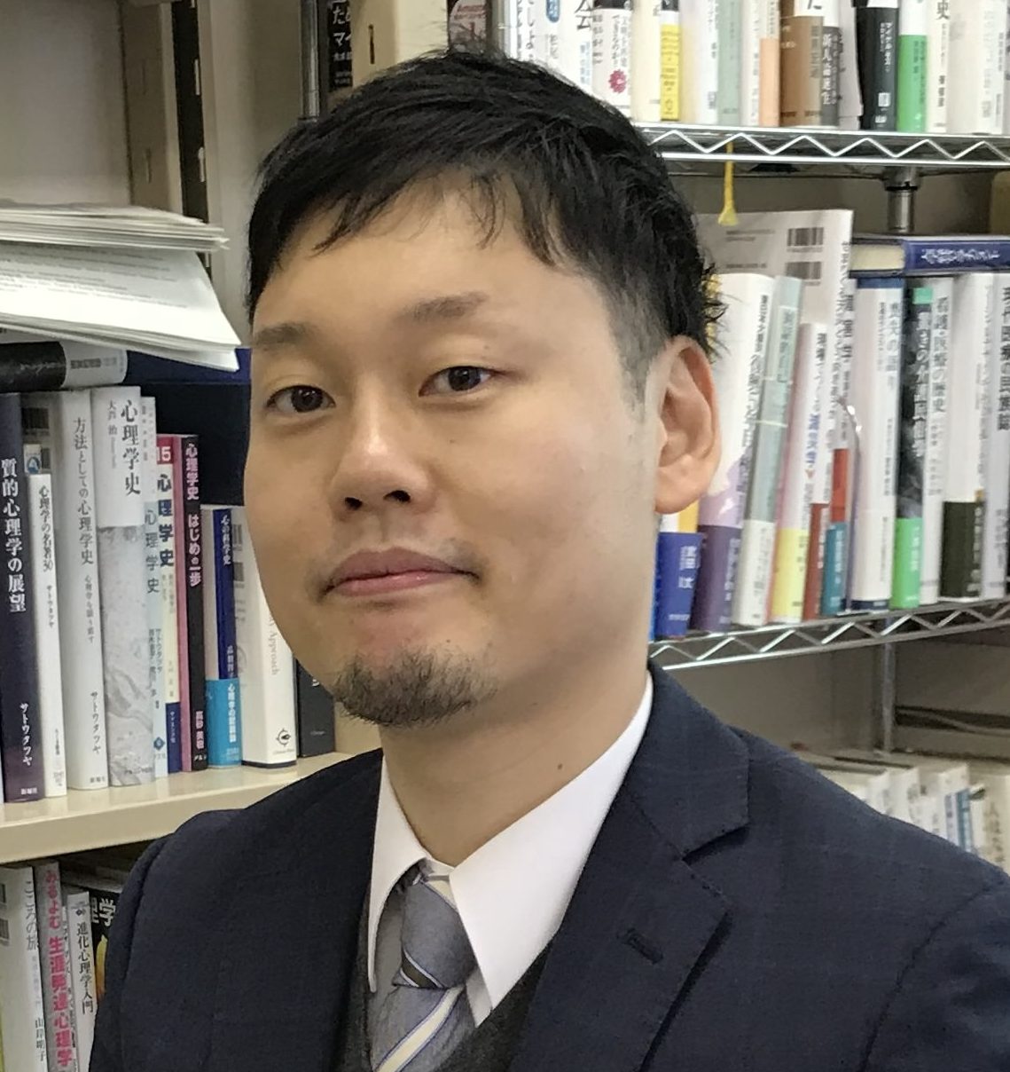 福島県立医科大学の講師、日高友郎氏が書斎で微笑む姿。背景には多くの書籍が並んでいる。