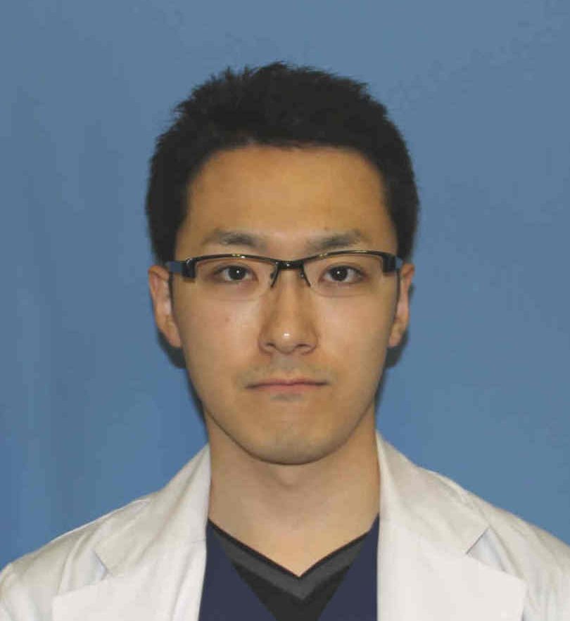 医療用白衣を着た男性のポートレート。背景は青色で、真剣な表情を浮かべている。