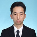 心房細動に関する研究を行う医師のポートレート。スーツを着用し、真剣な表情でカメラを見つめている。
