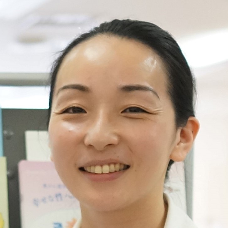 医療現場で微笑む女性医師のポートレート。背景には医療関連の資料が見える。