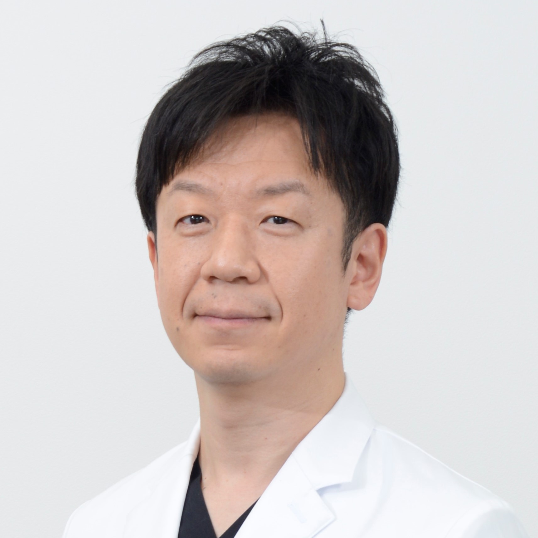 医療白衣を着た志賀哲也准教授のポートレート。背景はシンプルな白。