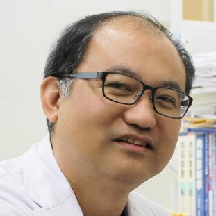 医療現場での研究者のポートレート。白衣を着た男性がカメラに微笑んでいる。