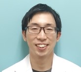 医療白衣を着た男性が微笑んでいるポートレート。背景は淡い青色。