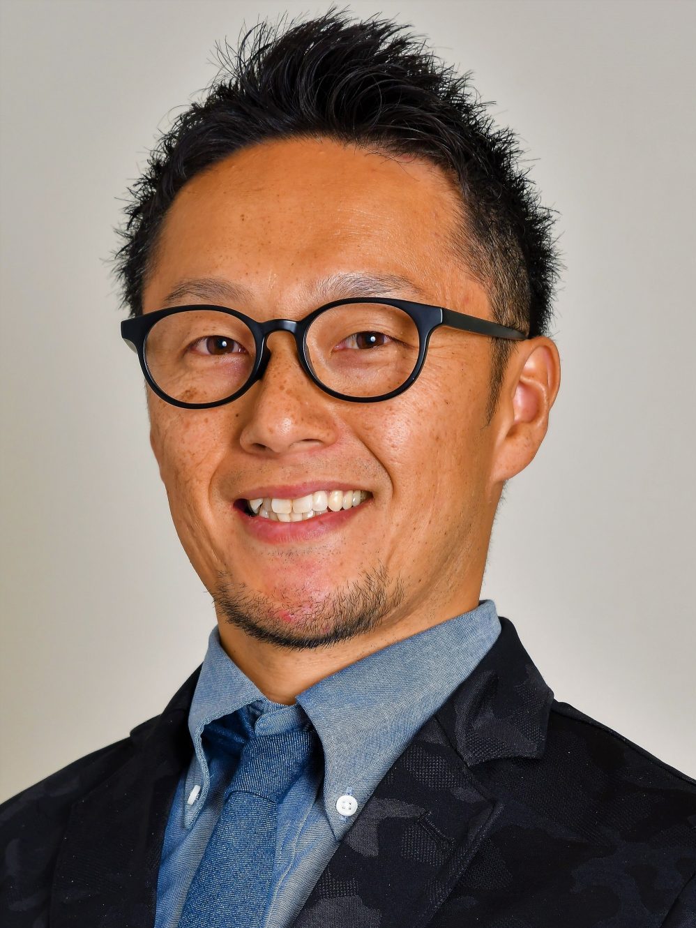 大前憲史氏のポートレート。眼鏡をかけた笑顔の男性がスーツを着用している。