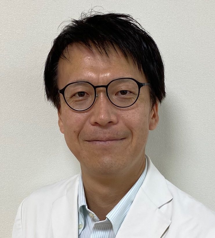医師の男性が白衣を着て微笑んでいるポートレート。背景はシンプルな壁。