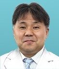 医療用白衣を着た男性が微笑んでいるポートレート。背景は淡い青色。