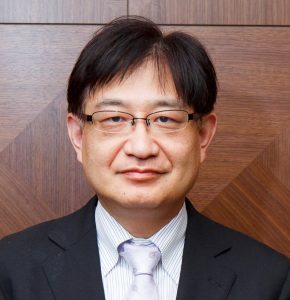 池田和彦教授がスーツを着て微笑んでいるポートレート。背景は木目調の壁。