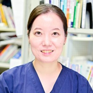 全身性エリテマトーデスに関する研究を行う医師が微笑んでいるポートレート。背景には書籍や資料が並ぶ。