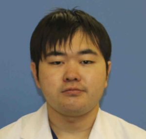 医療用白衣を着た男性の顔写真。背景は青色。