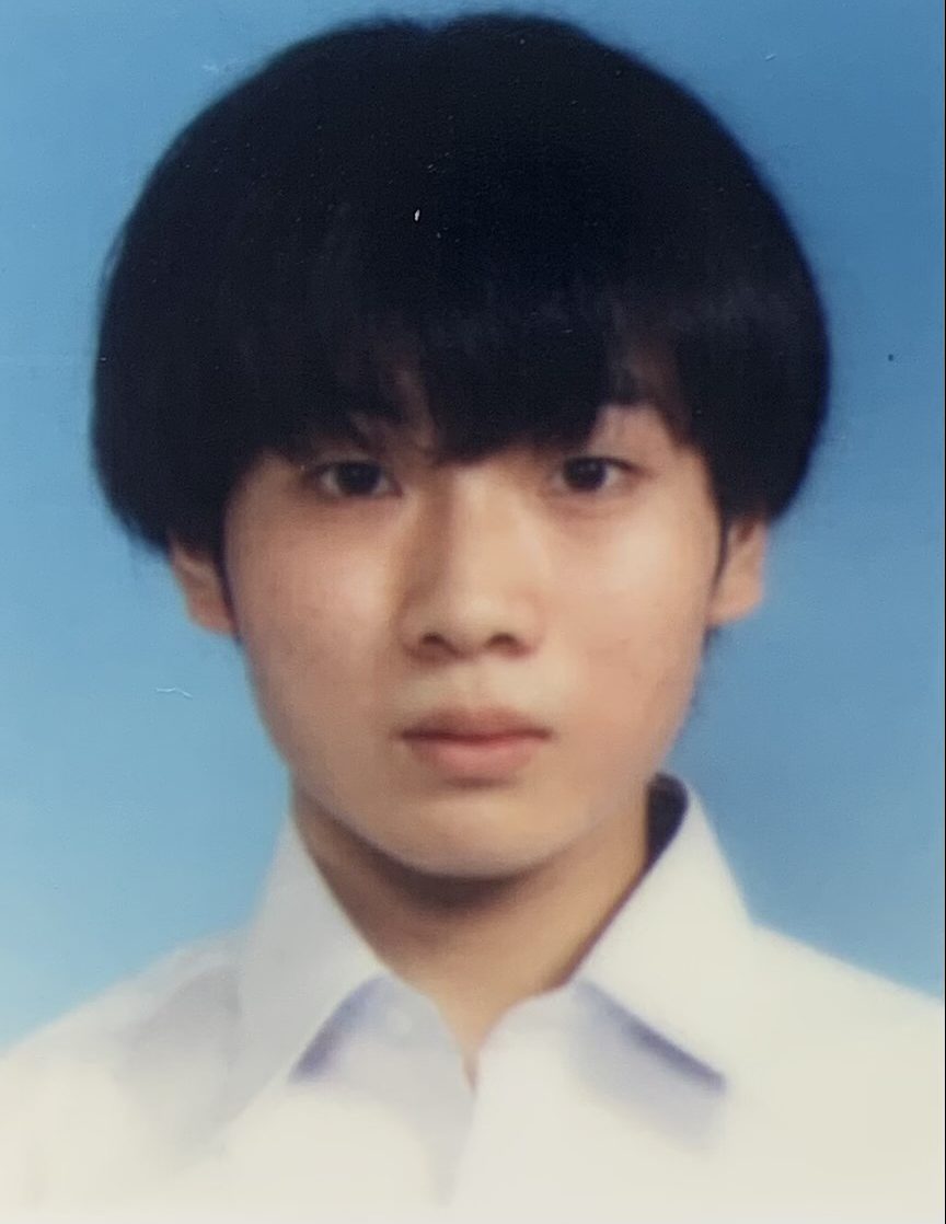 学生の制服を着た若い男性の顔写真。青い背景の前で真剣な表情を浮かべている。